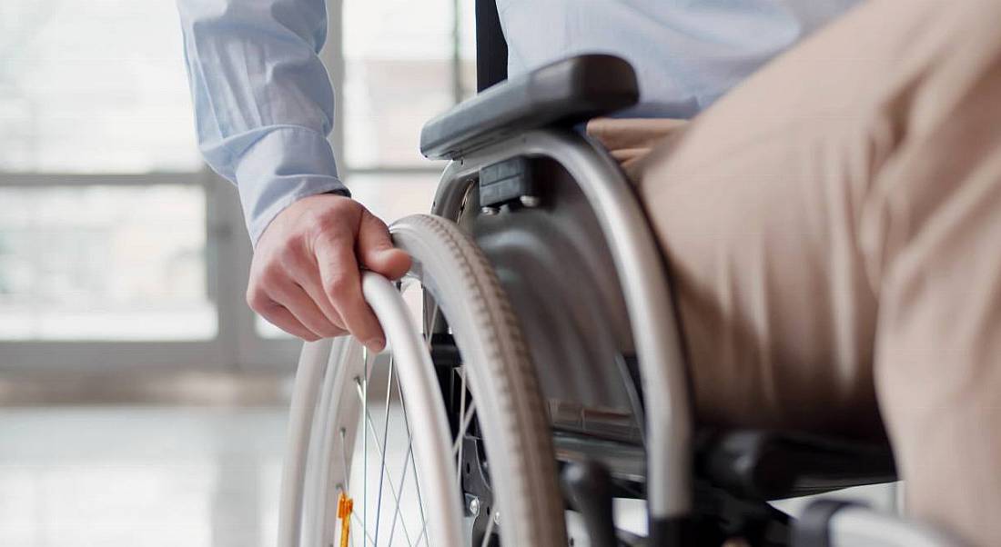 Close-up of a man's hand holding the wheel of his wheelchair as he enters an office.