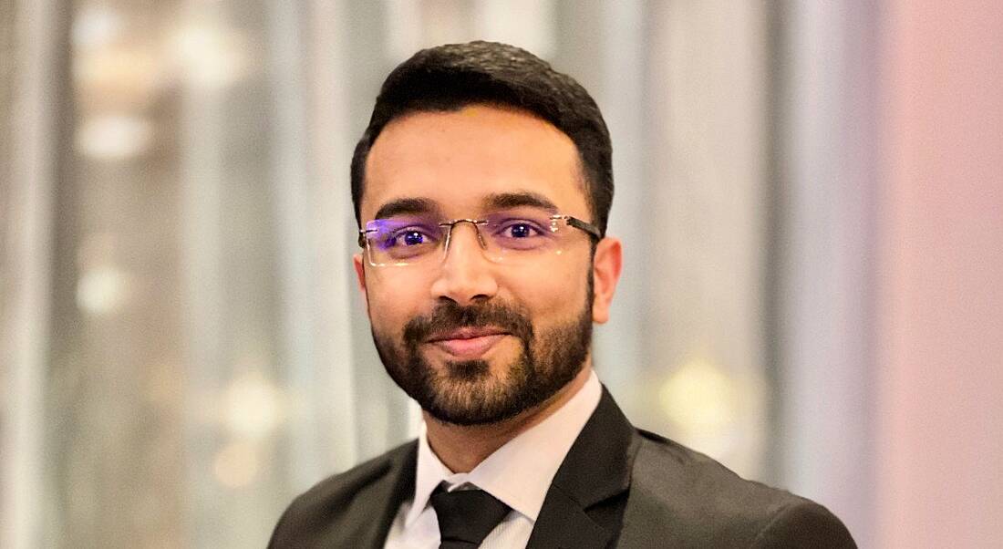 A young man wearing a suit and glasses smiling at the camera.