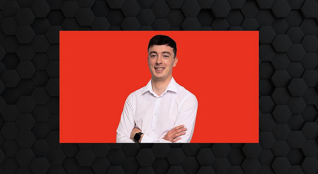 A headshot of Colin Hehir, a young man in a white shirt against a red background surrounded by a dark grey designed frame.