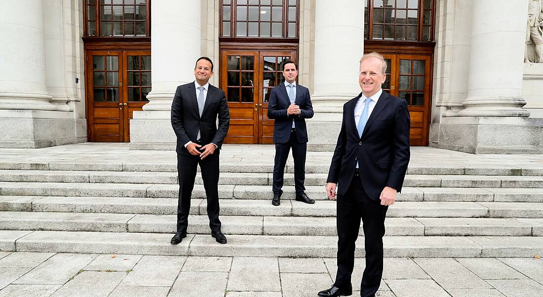 Three men in suits stand, socially distanced, on the steps of Government buildings.