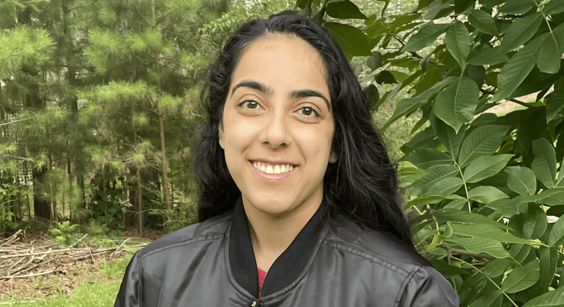 A close-up of a young woman, Jasmine Singh, who works at NASA as an intern. There are leafy trees in the background.