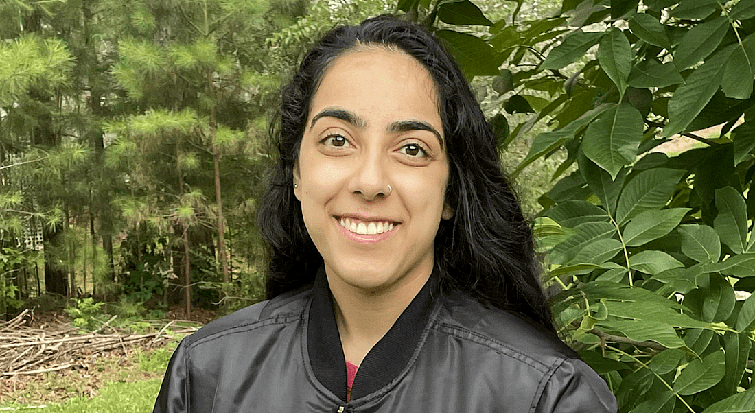 A close-up of a young woman, Jasmine Singh, who works at NASA as an intern. There are leafy trees in the background.