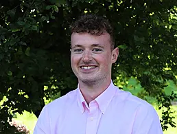 A young man wearing a suit and glasses smiling at the camera.