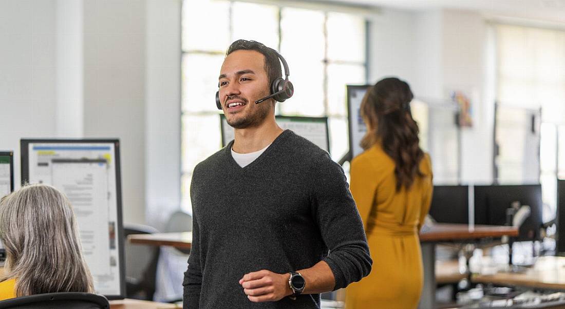 A person is walking through a bright office space, wearing a headset.