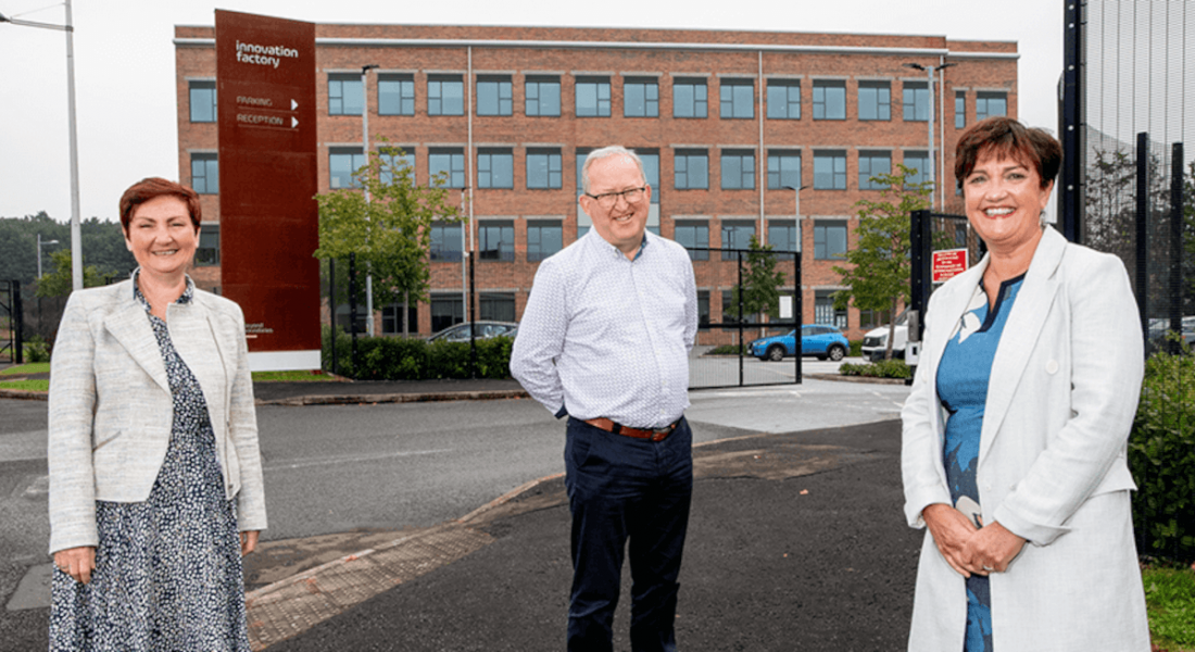 Photo of The Electric Company co-founders Anne Marie McGoldrick and Eddie McGoldrick with Grainne McVeigh of Invest NI, standing in front of the Innovation Factory in Belfast.