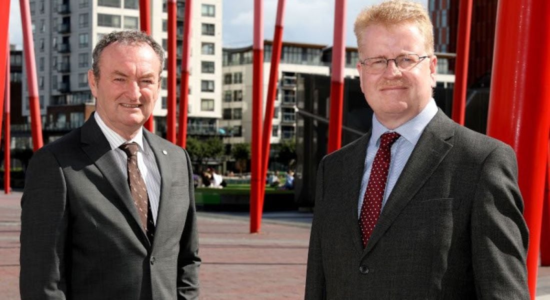 Tekenable managing director Nick Connors and CTO Peter Rose standing in Dublin's Grand Canal Dock with red sculptures behind them.