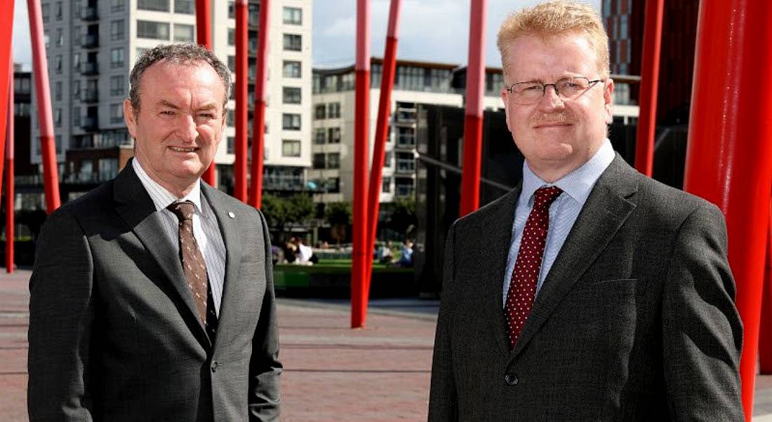 Tekenable managing director Nick Connors and CTO Peter Rose standing in Dublin's Grand Canal Dock with red sculptures behind them.