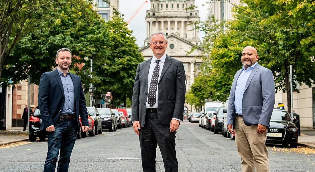 Three people stand distanced on a city street.