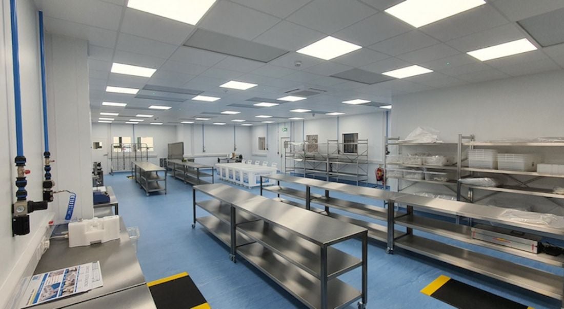 The Watson-Marlow facility is shown. There are long, steel tables throughout the room and laboratory equipment on shelves against the walls.