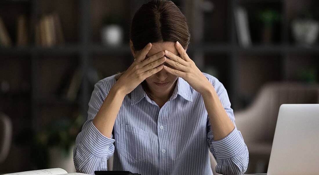 Young woman distressed with hand on head while working at a desk.