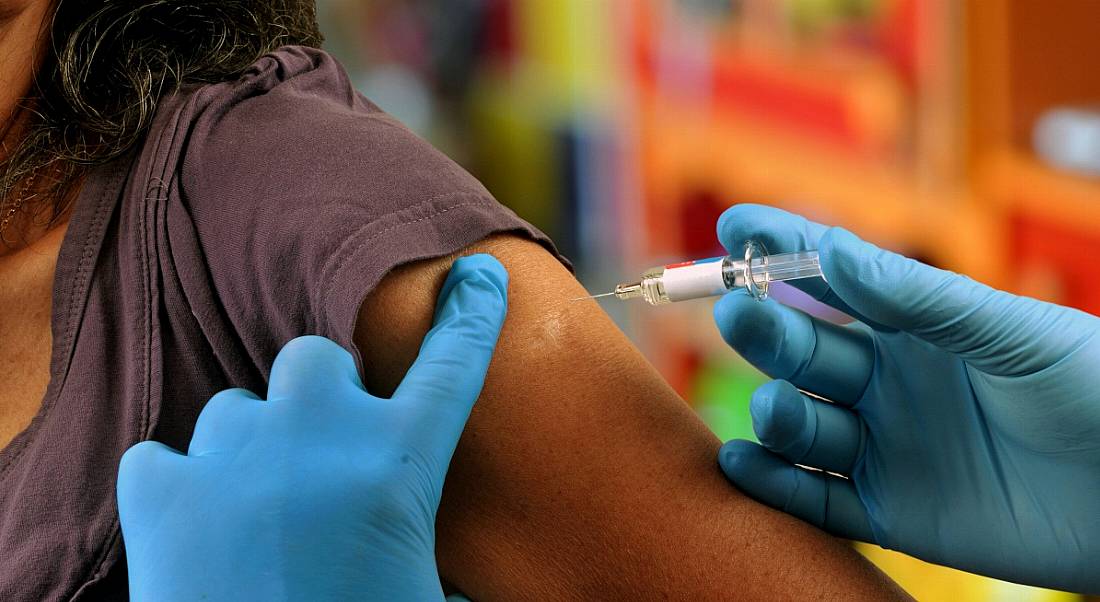 A woman is getting vaccinated by a health professional wearing blue surgical gloves.