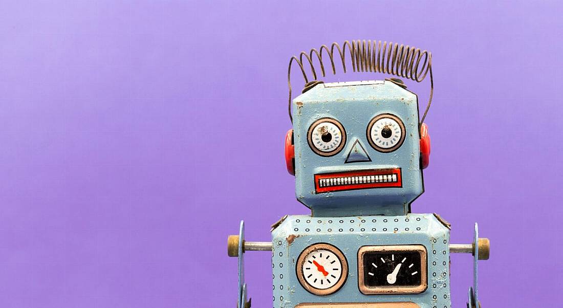 A vintage toy robot is standing against a purple background, symbolising automation and digital co-workers.