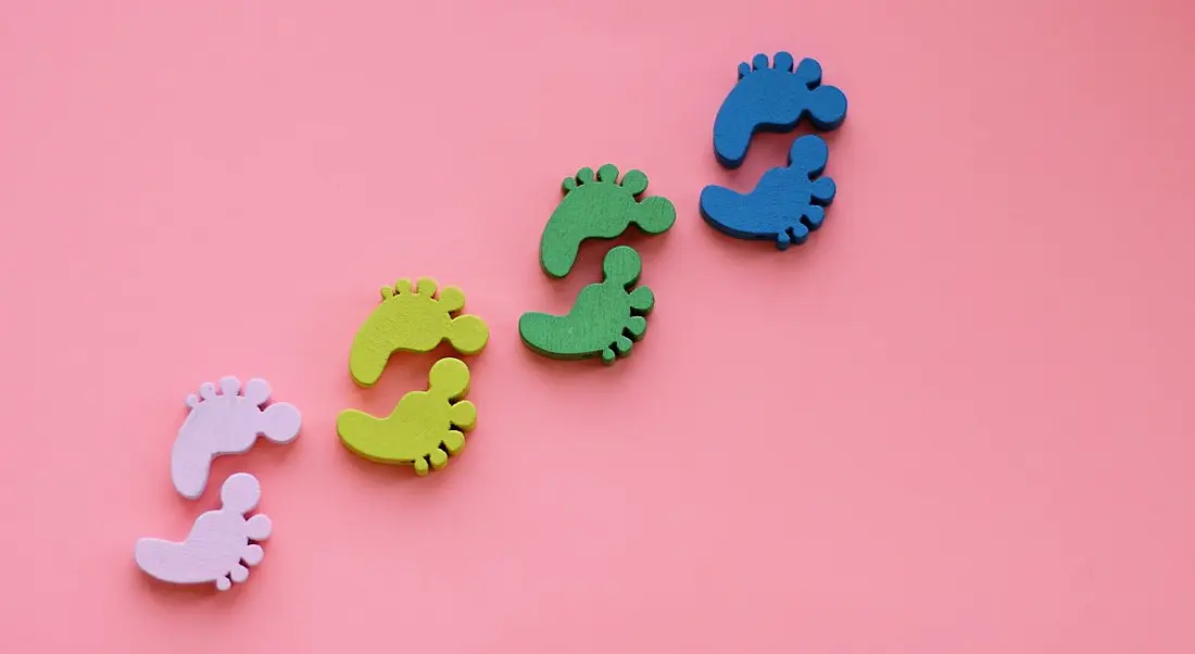 Pink, yellow, green and blue footprints against a pink background, symbolising first steps.