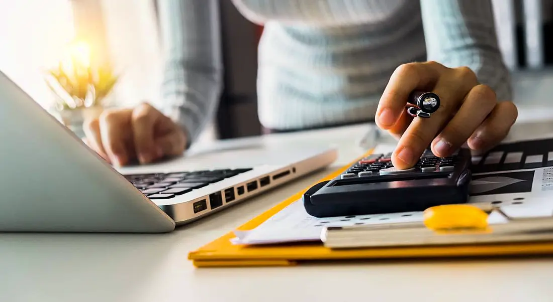 A woman is calculating her tax reliefs using a calculator and laptop.