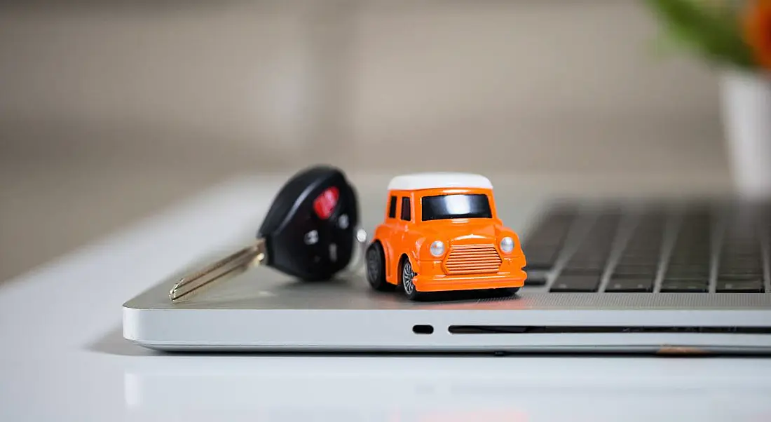 An orange toy mini cooper car is sitting next to a car key on a laptop.