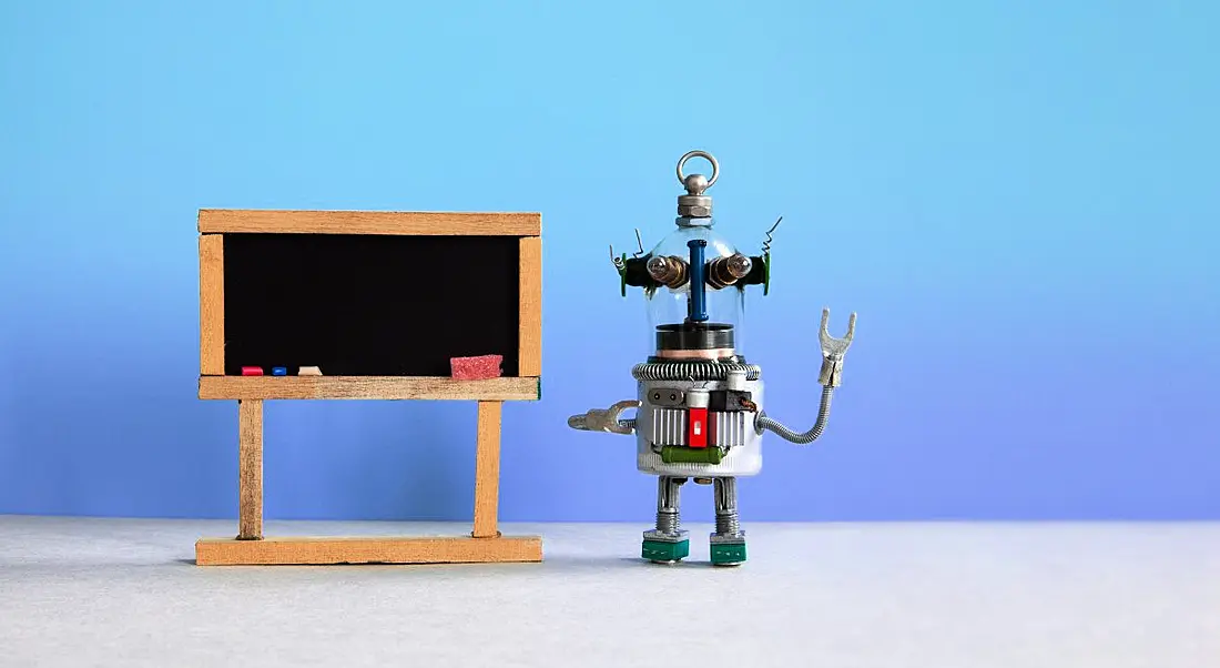 A toy robot is standing next to a blackboard against a blue background.