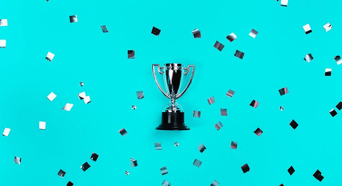 A silver trophy is laying against a blue background where it is surrounded by silver confetti.