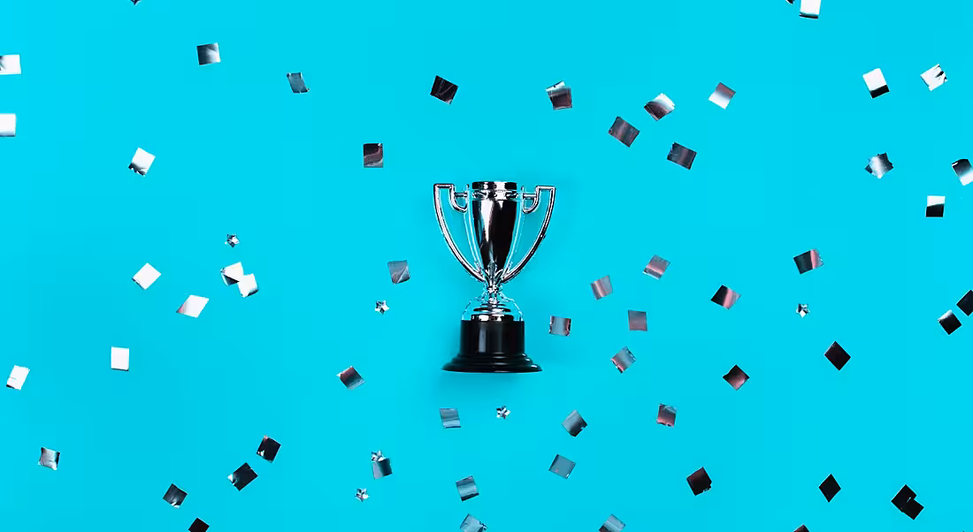 A silver trophy is laying against a blue background where it is surrounded by silver confetti.