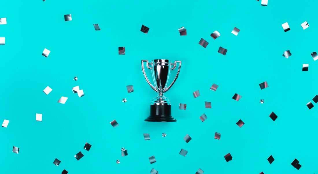 A silver trophy is laying against a blue background where it is surrounded by silver confetti.