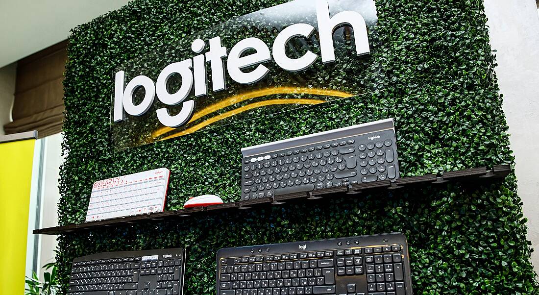 A wall display of four computer keyboards against a backdrop of greenery. The Logitech logo is displayed above the keyboards.