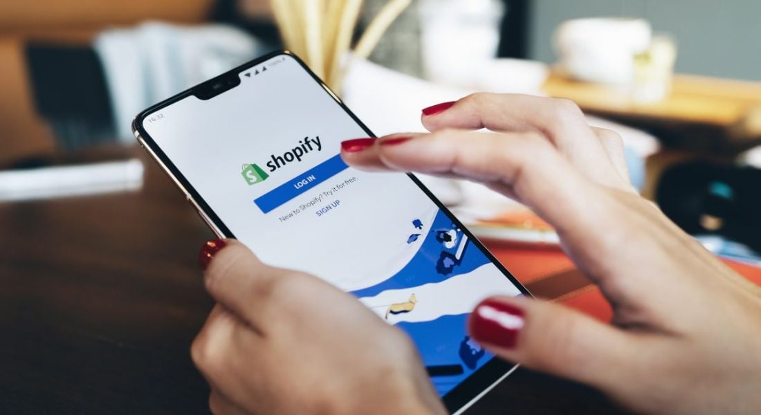 A woman is using a phone with the Shopify app open on it.