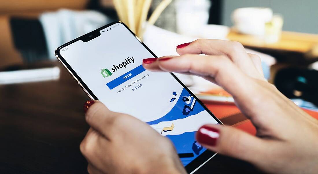 A woman is using a phone with the Shopify app open on it.