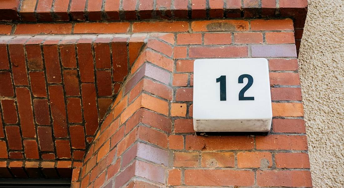 A number 12 sign on a brick wall of a house, beside the front door.