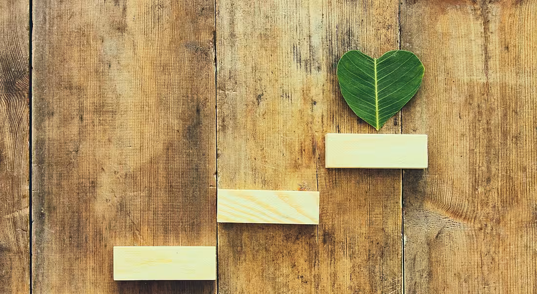 Wooden steps are leading up to a heart-shaped leaf against a wooden background.