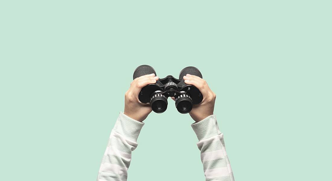 Hands are holding up binoculars against a plain green background.