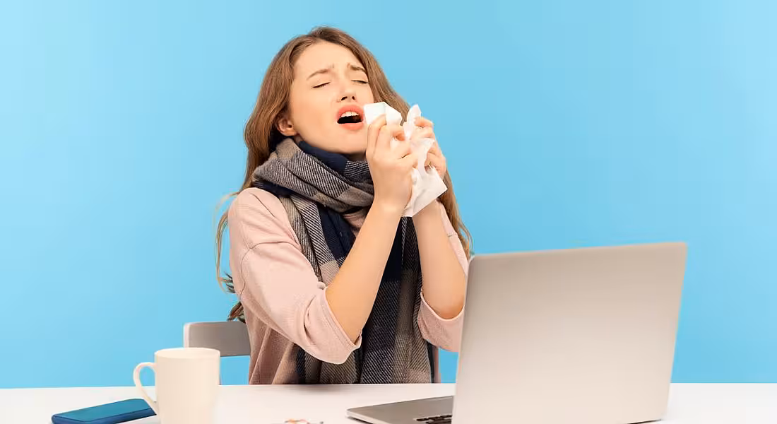 A woman is sneezing while working on her laptop.