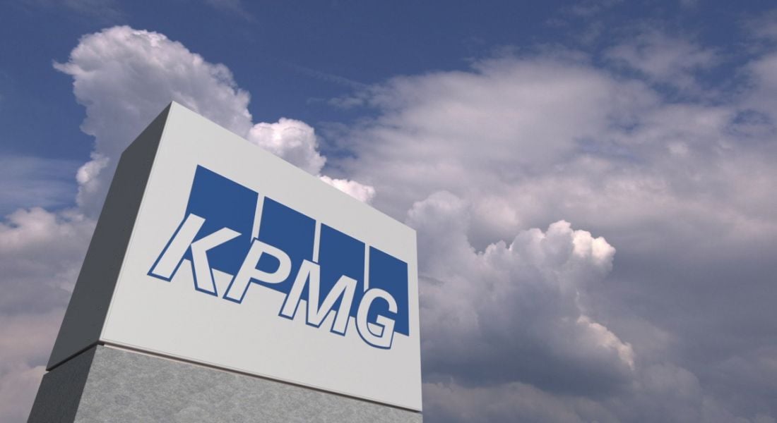 A KPMG company sign is photographed against a blue sky with clouds.