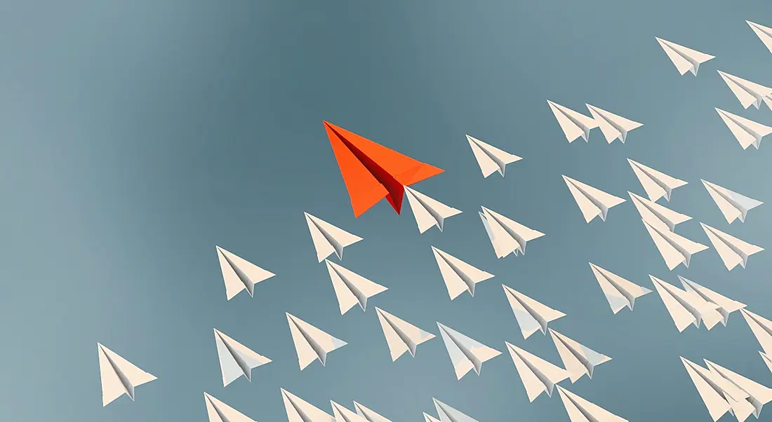 An illustration of a red paper plane flying ahead of a bunch of white paper planes, symbolising leadership.