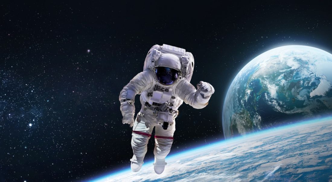 An astronaut is floating in space with the Earth and moon visible behind them.