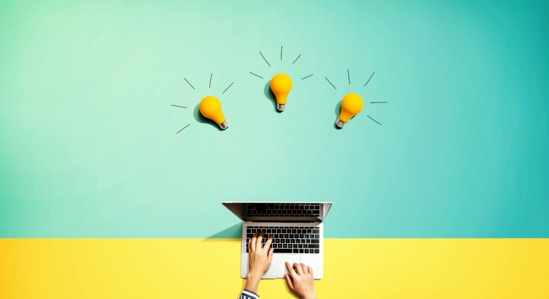 Person using a laptop computer with three lightbulbs lying above it against a yellow and bright blue background.