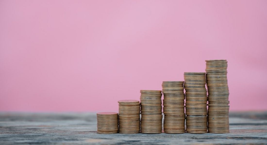 Stacks of coins are growing higher one after the other against a pink background, symbolising pay rises.