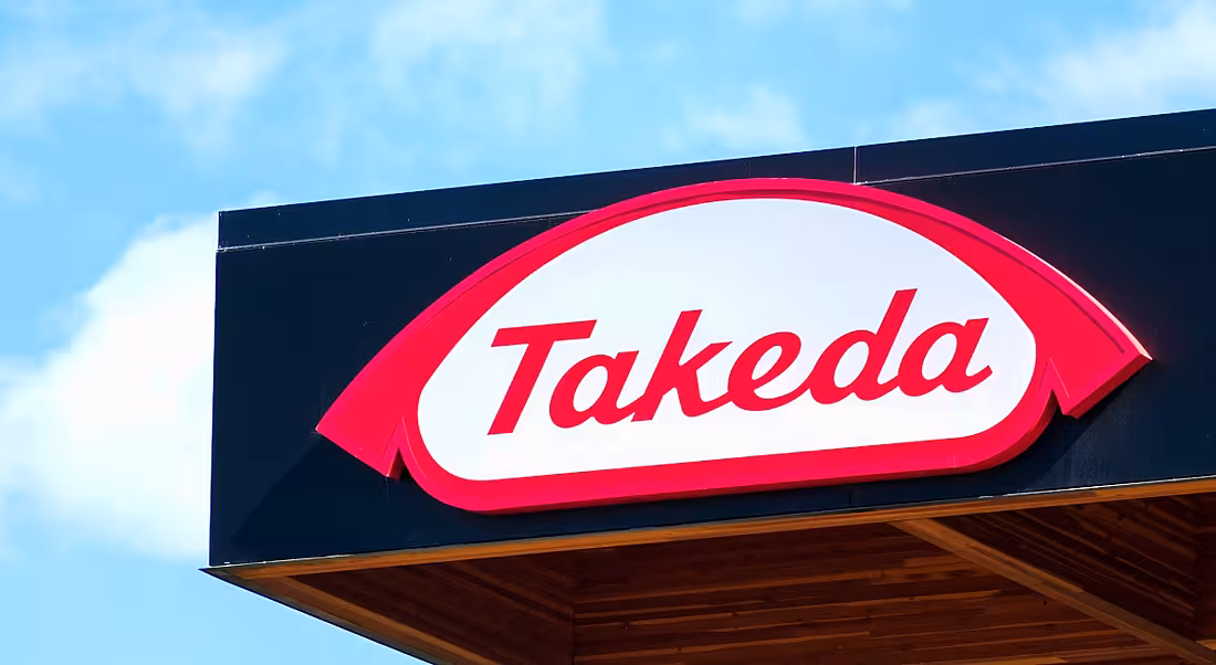 A sign of the Takeda logo on the top of an office building against a blue sky.