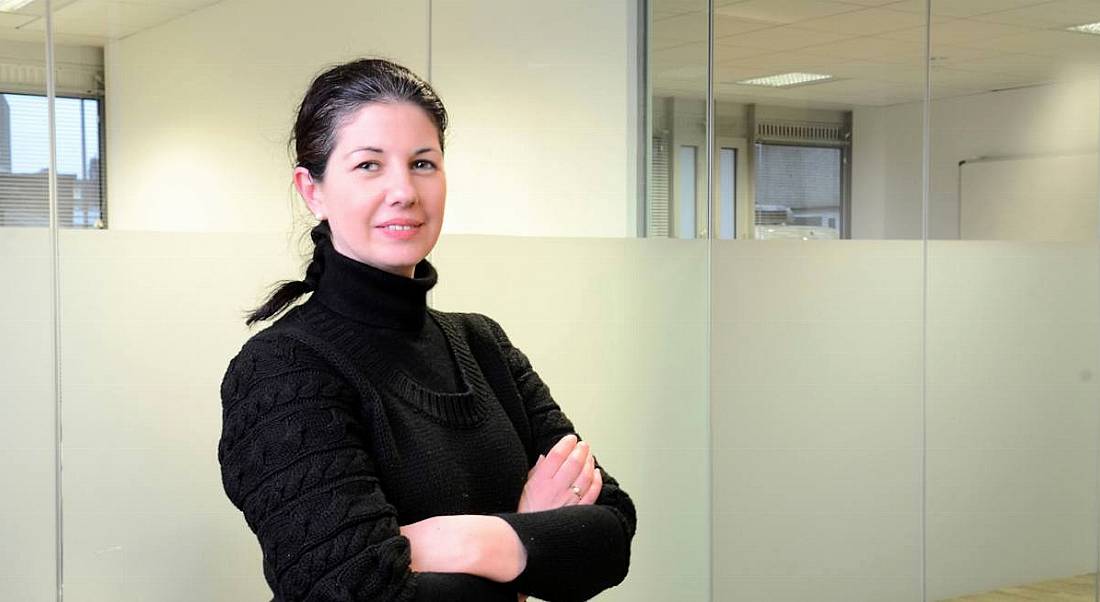 Miriam Byrne of Triangle is standing in an office space with her arms folded, smiling into the camera.