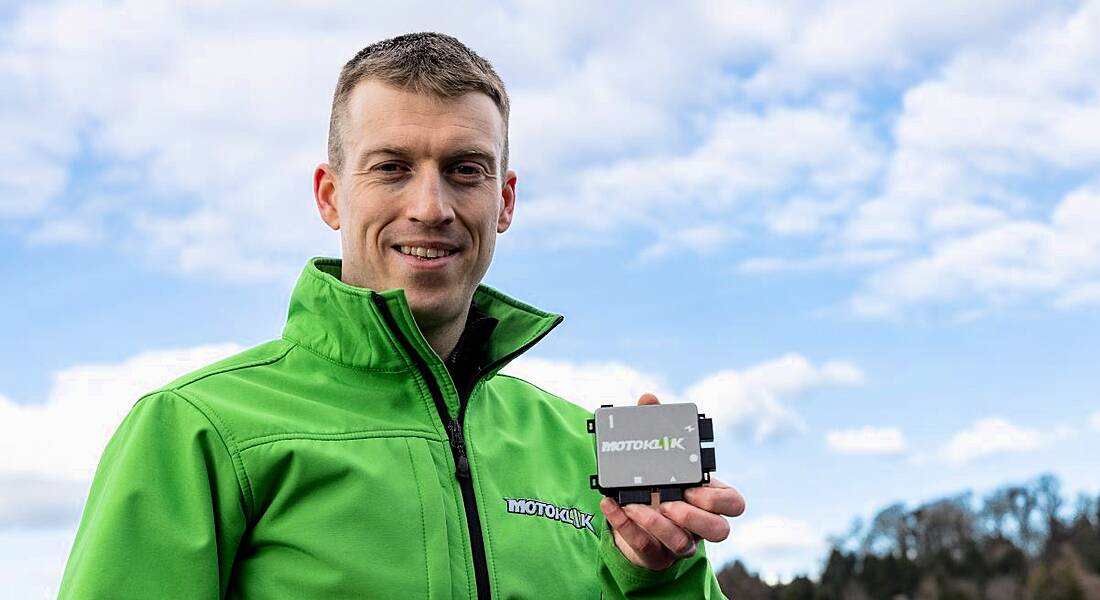 Jens Köpke holds up the palm-sized Motoklik device. He is wearing a high-vis green jacket.