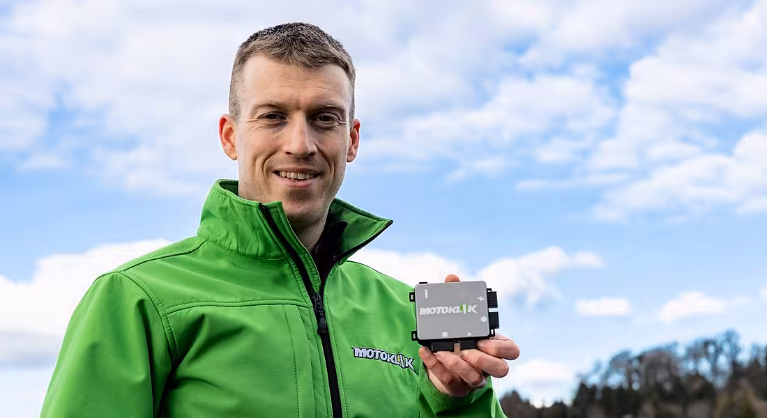 Jens Köpke holds up the palm-sized Motoklik device. He is wearing a high-vis green jacket.