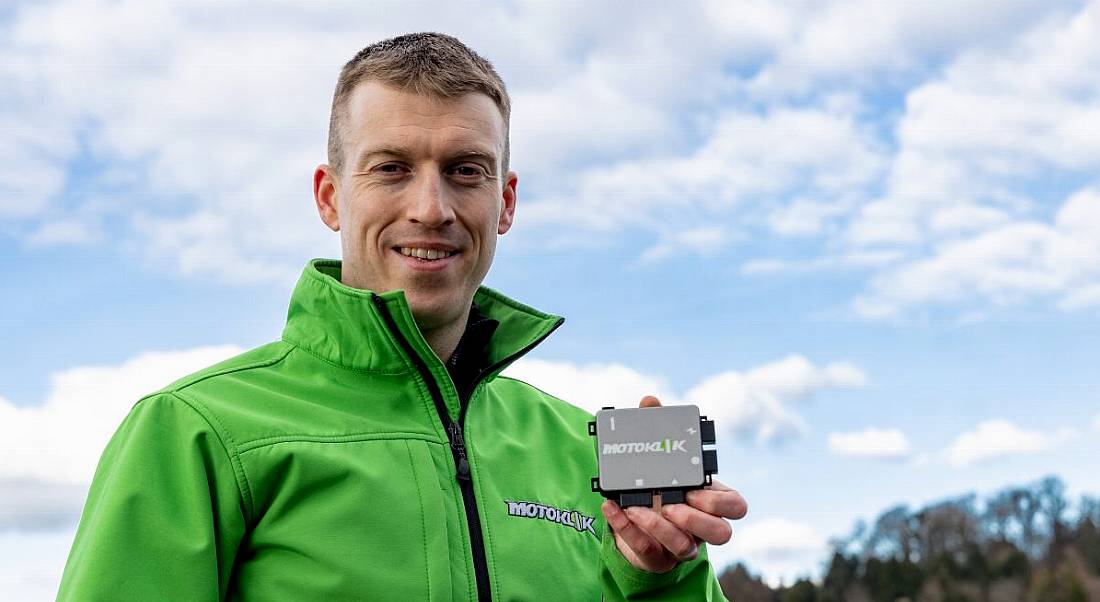 Jens Köpke holds up the palm-sized Motoklik device. He is wearing a high-vis green jacket.