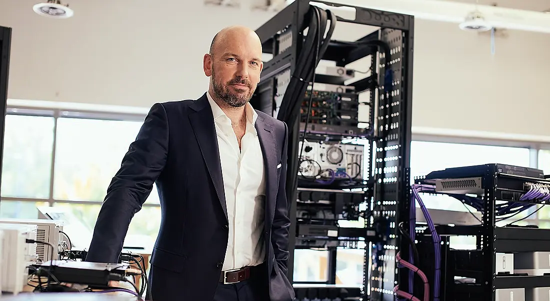 Okto managing director Philip Dowds is standing in a room with air-filtration technology behind him as he looks into the camera.