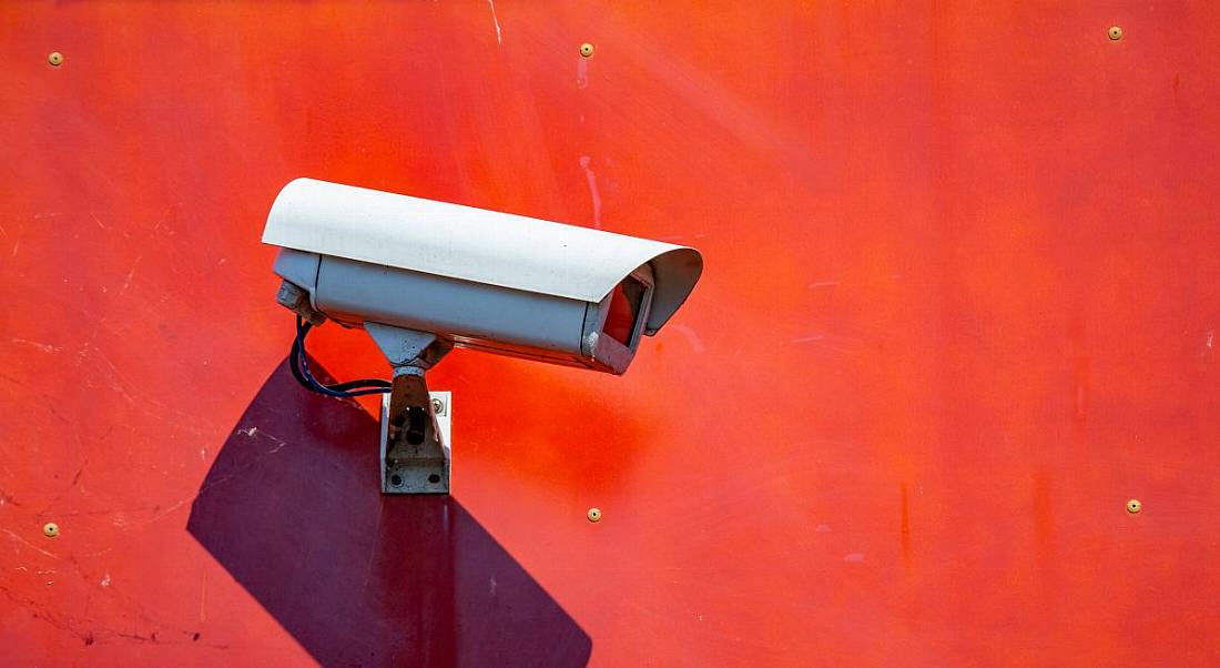 A security CCT camera mounted on a red-painted wall, symbolising workplace surveillance.