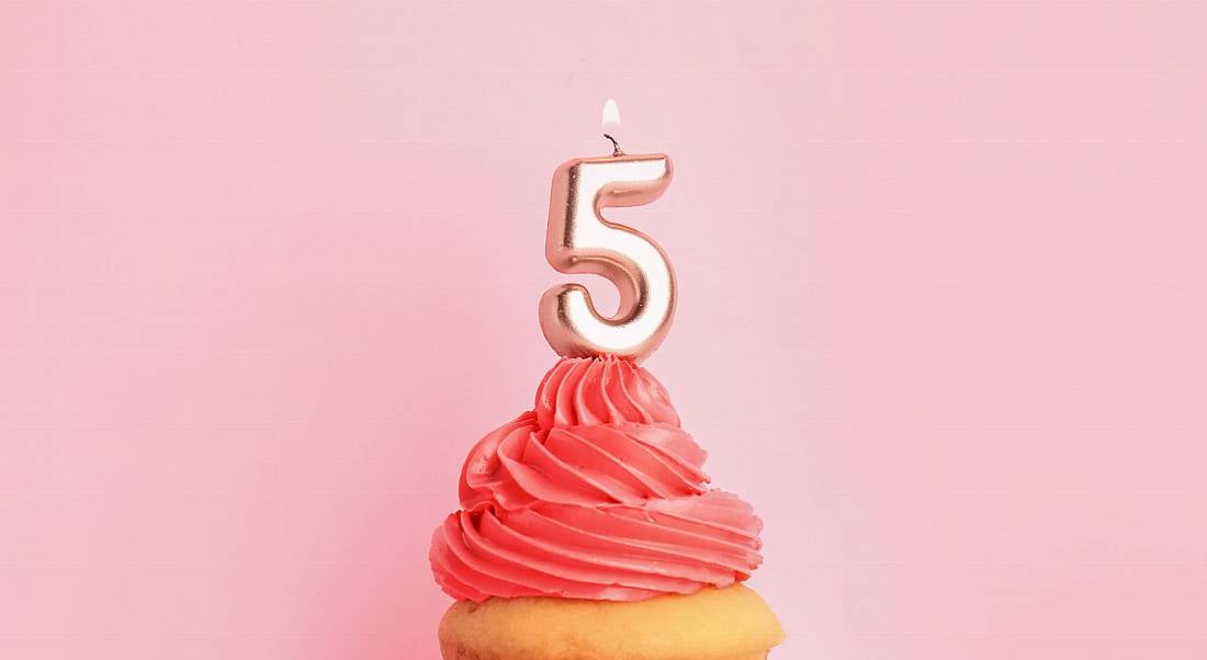 Birthday cupcake with number five candle on pink frosting against a pink background.