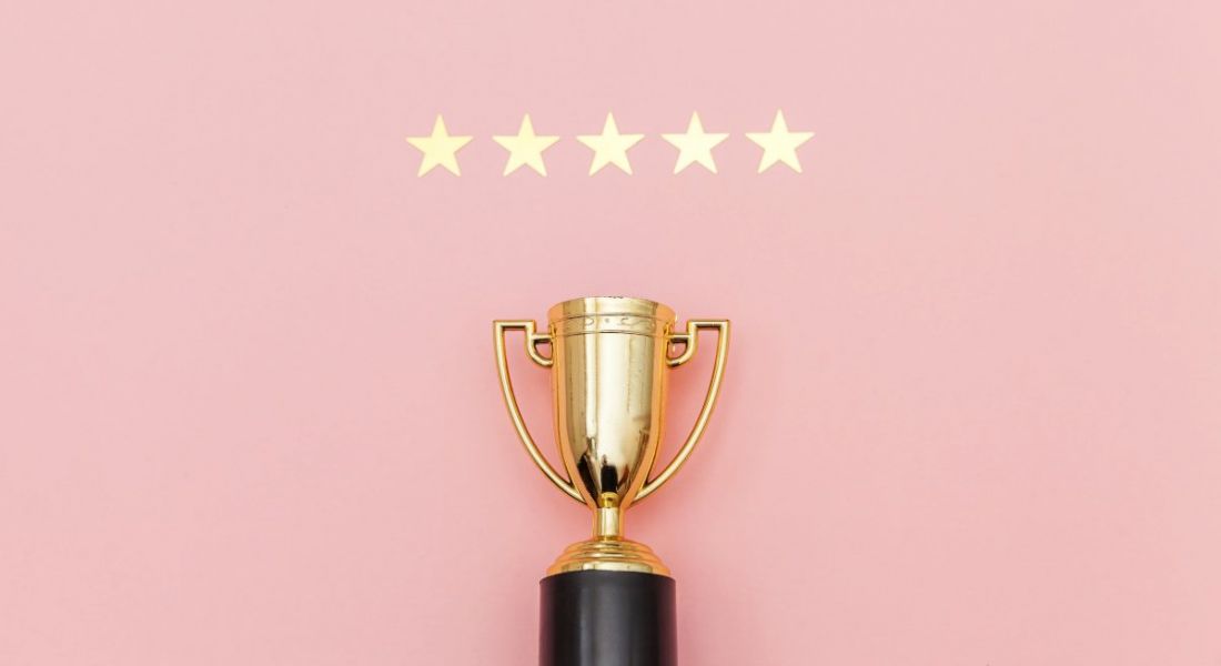 A gold trophy is resting below five gold stars against a light pink background.