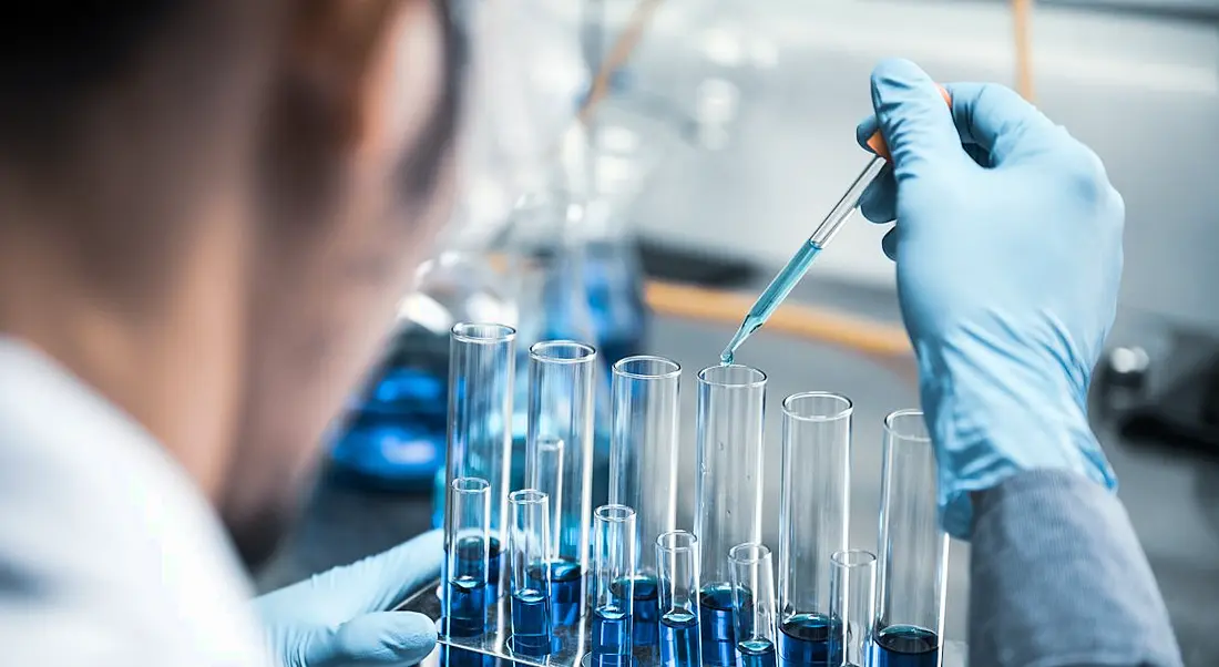 A life sciences employee is using a pipette to transfer chemicals in a lab setting.