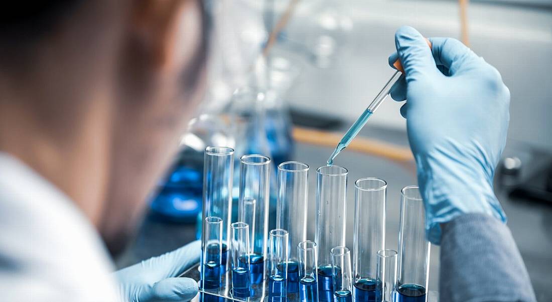 A life sciences employee is using a pipette to transfer chemicals in a lab setting.