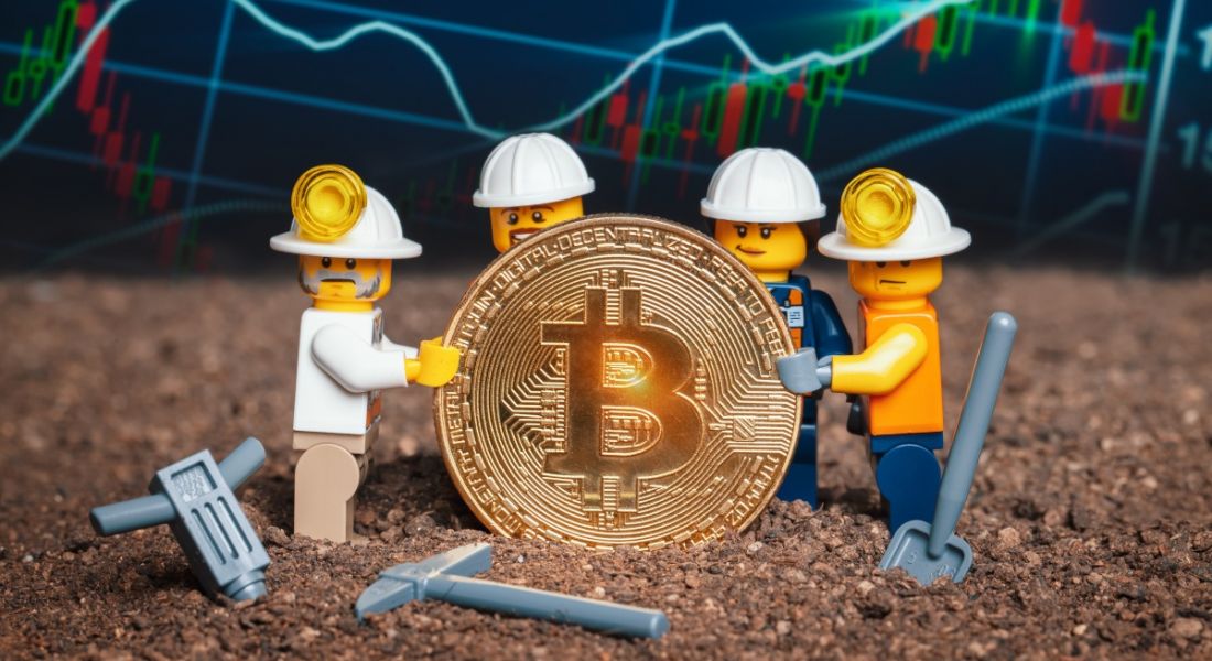 Group of Lego mini miner figurines holding shiny bitcoin together and posing, symbolising the role of a bitcoin programmer or bitcoin engineer.