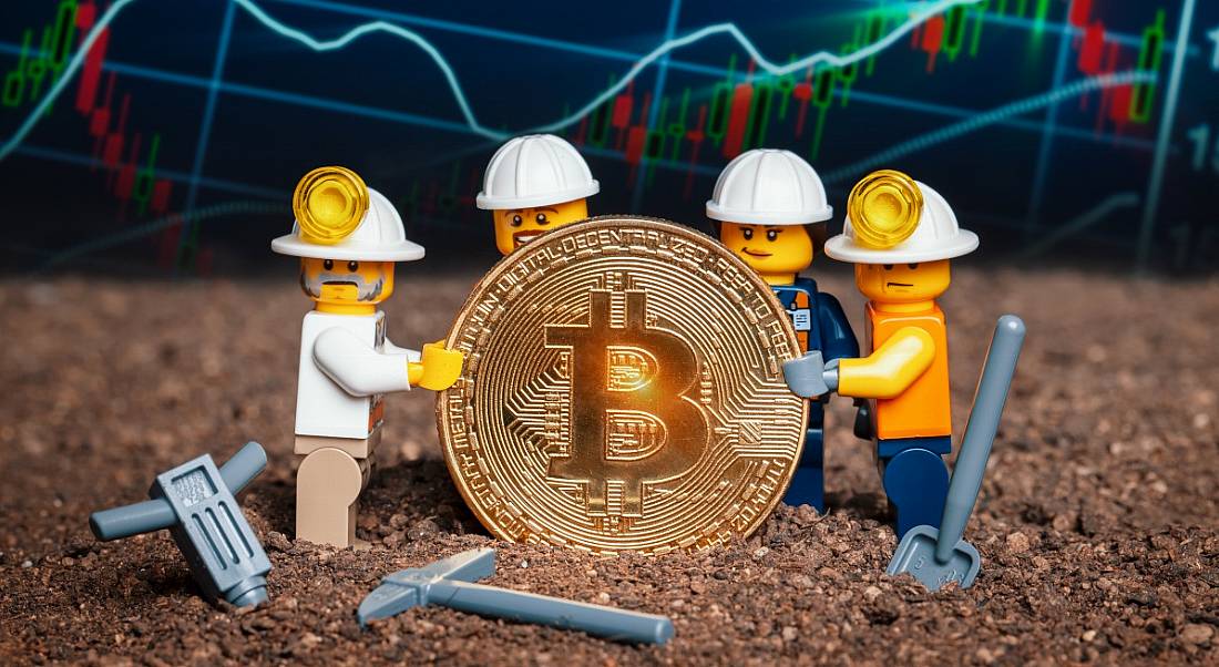 Group of Lego mini miner figurines holding shiny bitcoin together and posing, symbolising the role of a bitcoin programmer or bitcoin engineer.