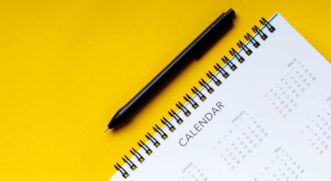 A pen lies beside a ring-bound full-year calendar on a sunflower yellow surface.