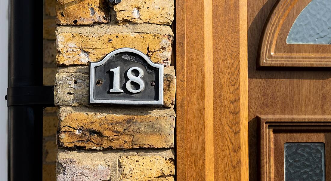 A sign with the number 18 on a brown brick wall next to the front door of a house.